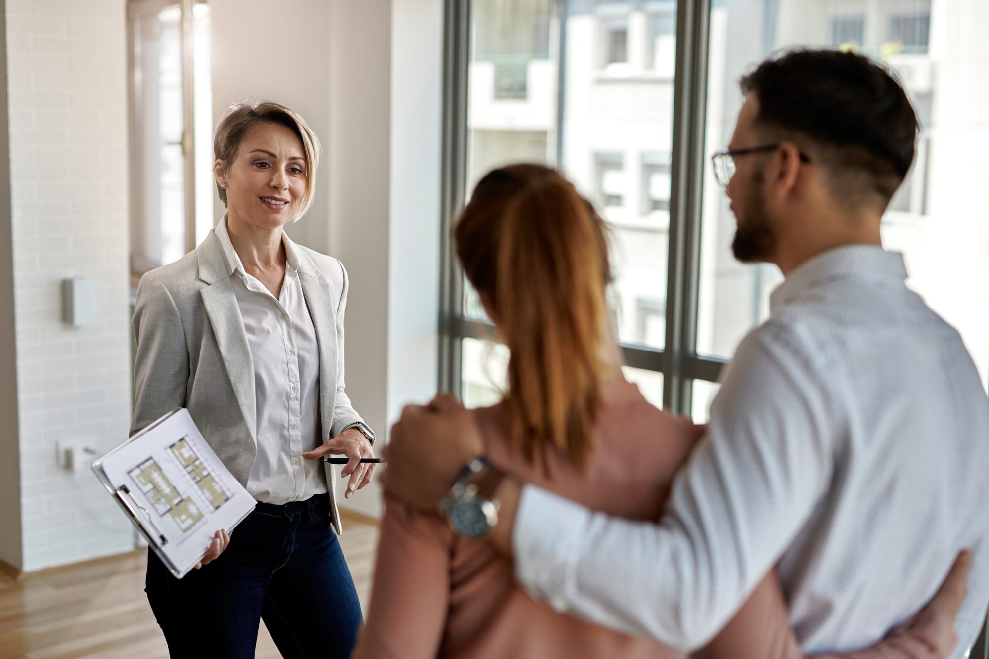 female-real-estate-agent-communicating-with-couple-while-showing-them-new-apartment-scaled